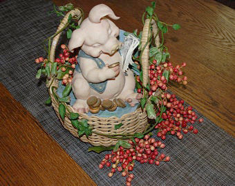 This is a pig in a wicker basket decorated with pink and red berries and green vines.